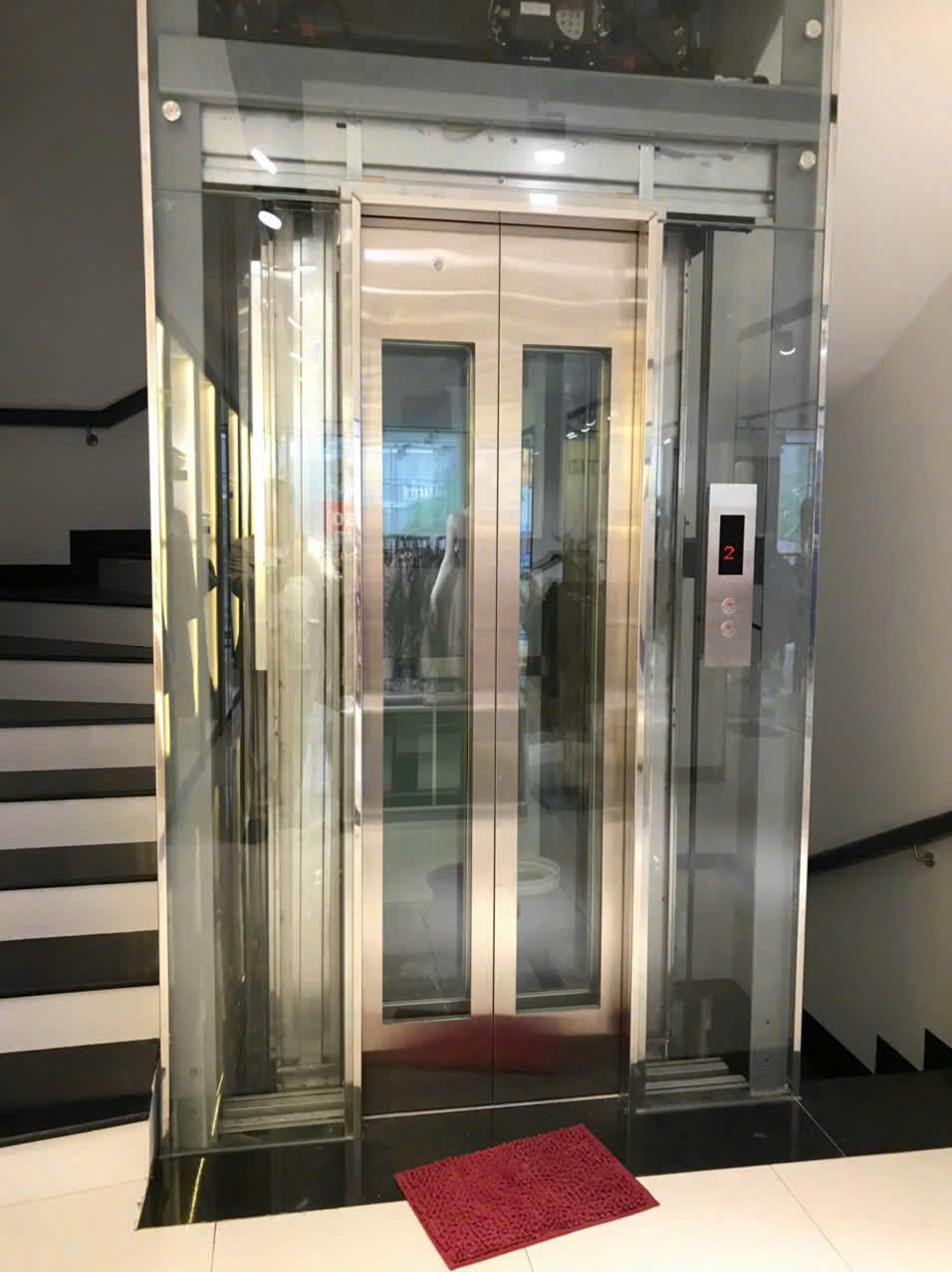 Thang máy kính gia đình cửa inox hai cánh mở giữa, bảng điều khiển hiển thị tầng 2